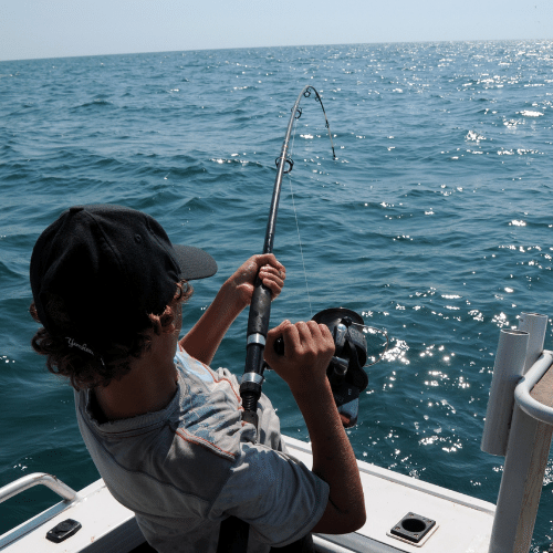 Man fishing on a boat in the ocean under clear sky, using fishing gear