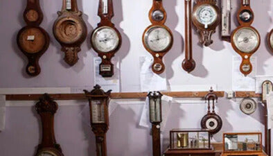 Wall display of vintage wooden barometers, clocks, and weather instruments.