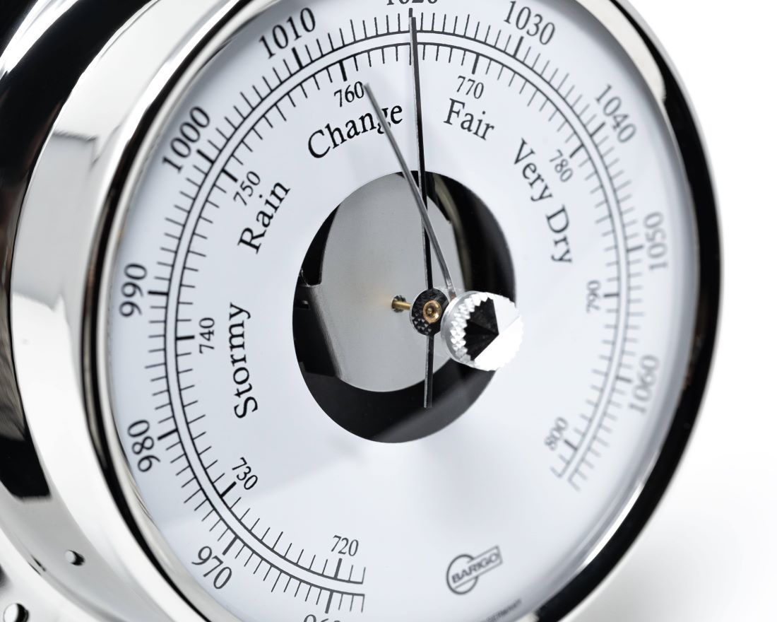 Close-up of a classic round barometer dial with metallic frame and clear weather markings.