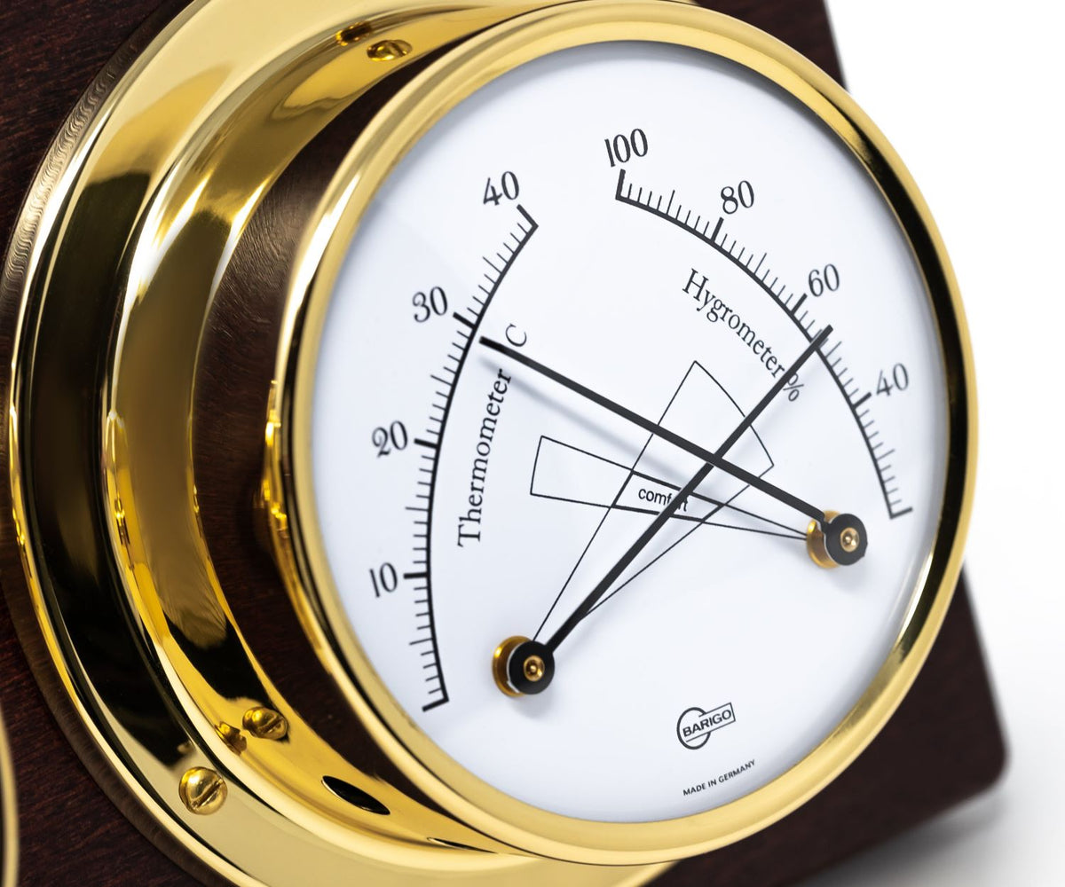 Close-up of a gold German made analog thermometer and hygrometer with white dial on wood base