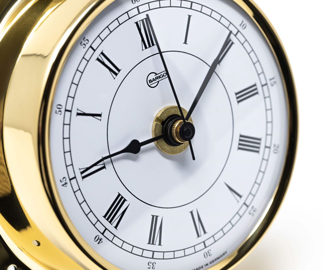 Close-up of gold-rimmed analog clock with Roman numerals and white face, nautical style.