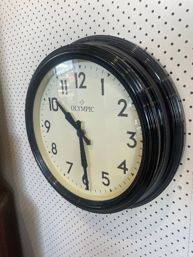 Black framed wall clock with white dial and bold numbers mounted on a pegboard wall
