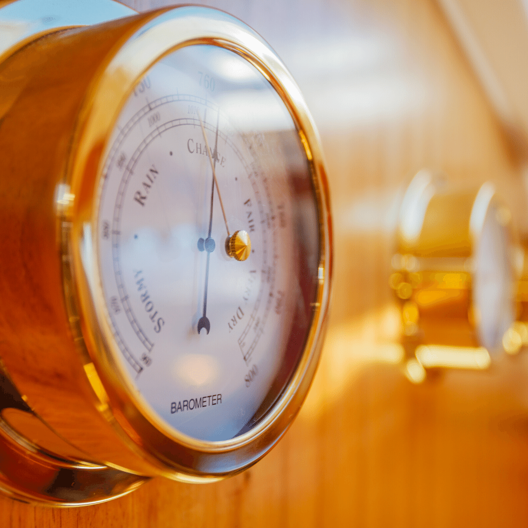 Gold analog barometer mounted on wood, close-up, nautical weather instrument