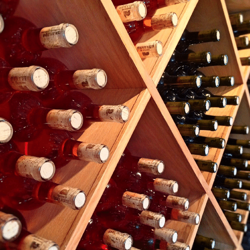 Wooden wine rack holding rows of red and white wine bottles in a cellar setting