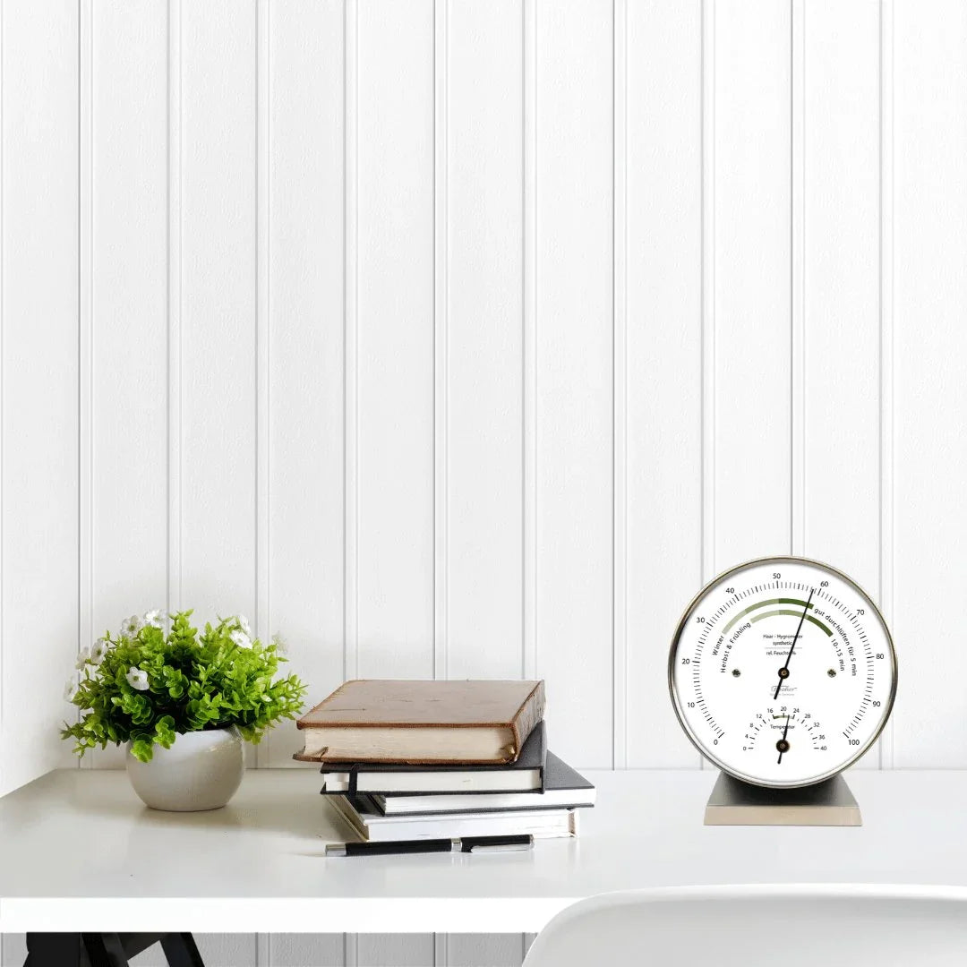 German barometer and hygrometer on white desk with books and potted plant, weather instrument