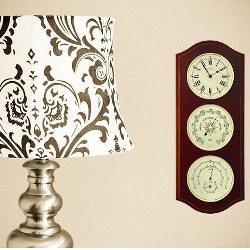 Wall-mounted German weather station with clock, barometer, hygrometer beside decorative lamp
