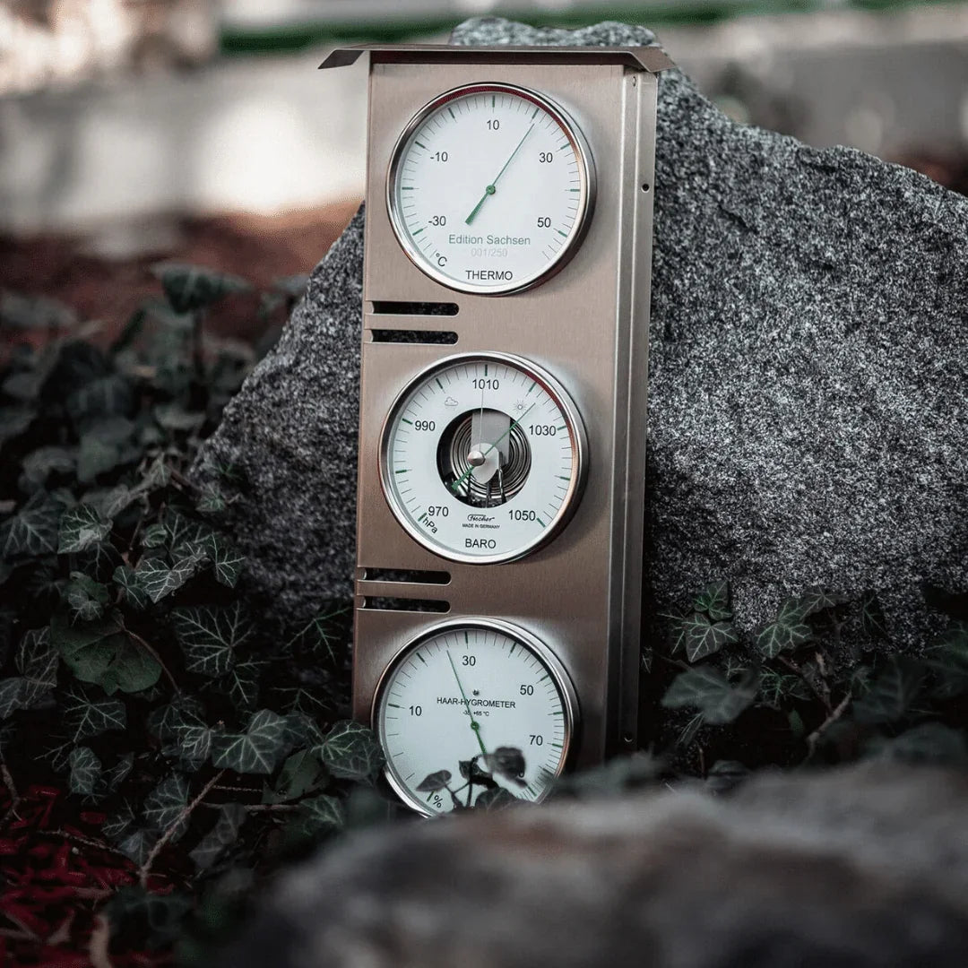 Triple gauge indoor thermometer, barometer, and hygrometer in metal case on rocks outdoors